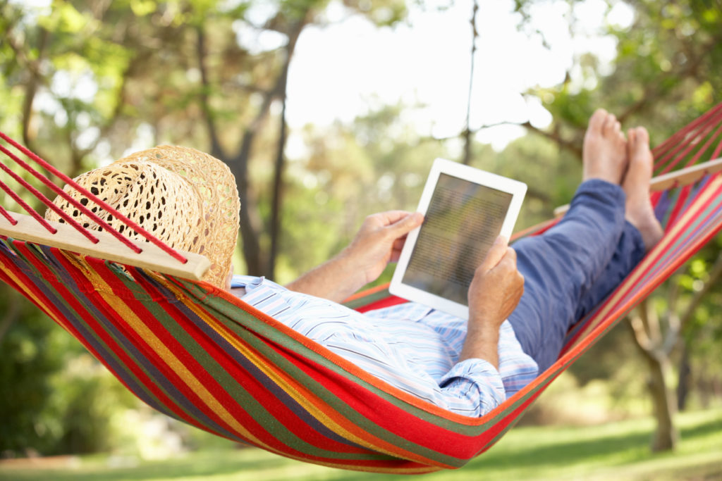 Man laying in hammock reading on tablet