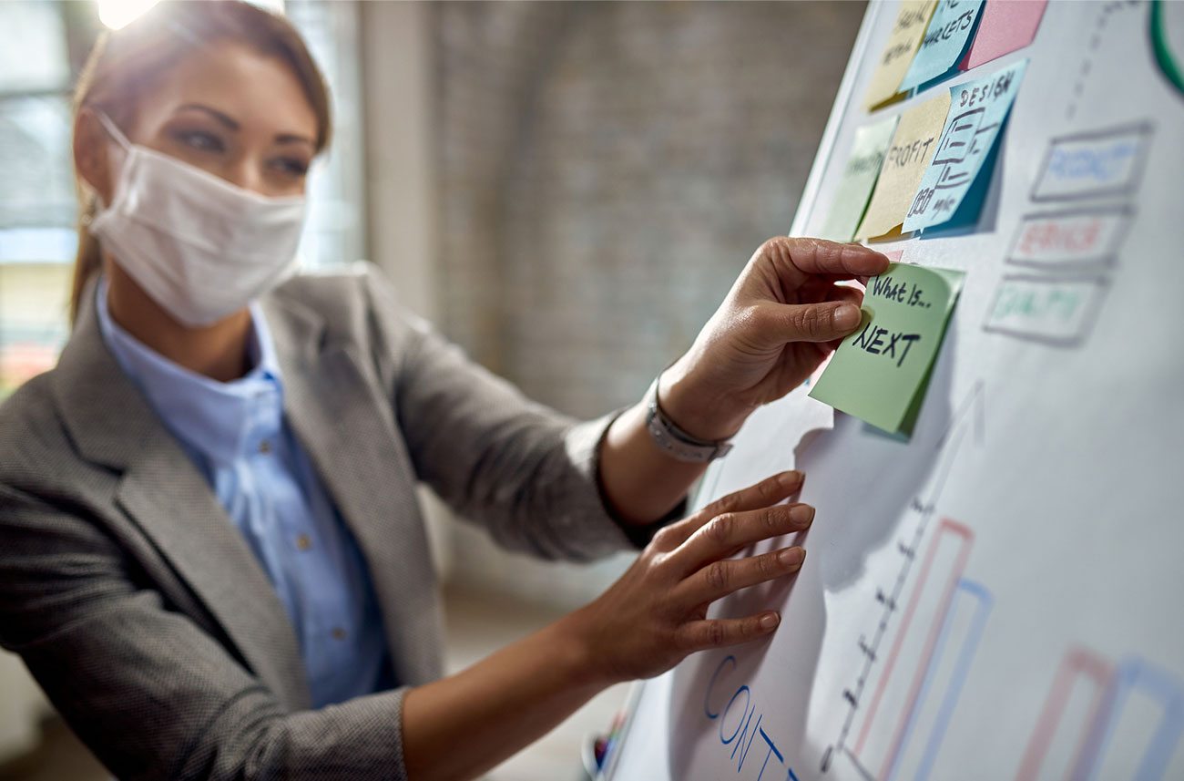 woman wearing face mask in office working on a white board with sticky-notes