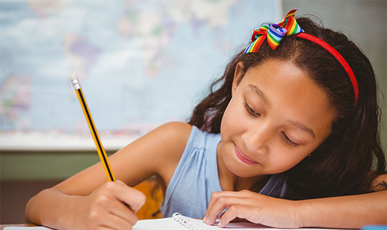 Girl writing in notebook with pencil at school