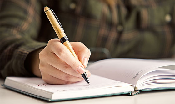 Person writing in calendar with wood gran pen