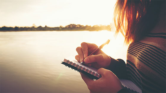 Woman writing in spiral bound notebook outside during sunset